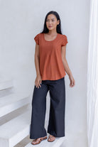 Woman wearing a rust-colored cotton summer top and dark pants standing on a white staircase.