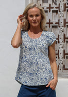 Woman wears a white based floral cotton cap sleeve top with pin tuck detail across the bust and a scoop neckline