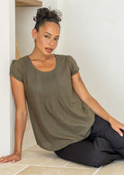 Woman wearing an olive green cotton cap sleeve top sitting on a tiled floor.