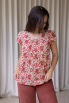Woman wearing a gentle cream based floral print short sleeve top with scoop round neckline and pleated detail across the bodice