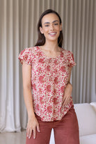 Woman wears cream based floral print 100% cotton cap sleeve top with pin tuck detail across the bust and a scoop neckline