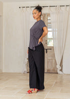 Woman wearing a gray top and black pants standing in a room with white curtains and a wooden door.