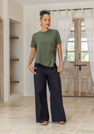 Woman wearing an olive green crew-neck twist-knot T-shirt in soft stretch rayon, styled with black cotton pants.