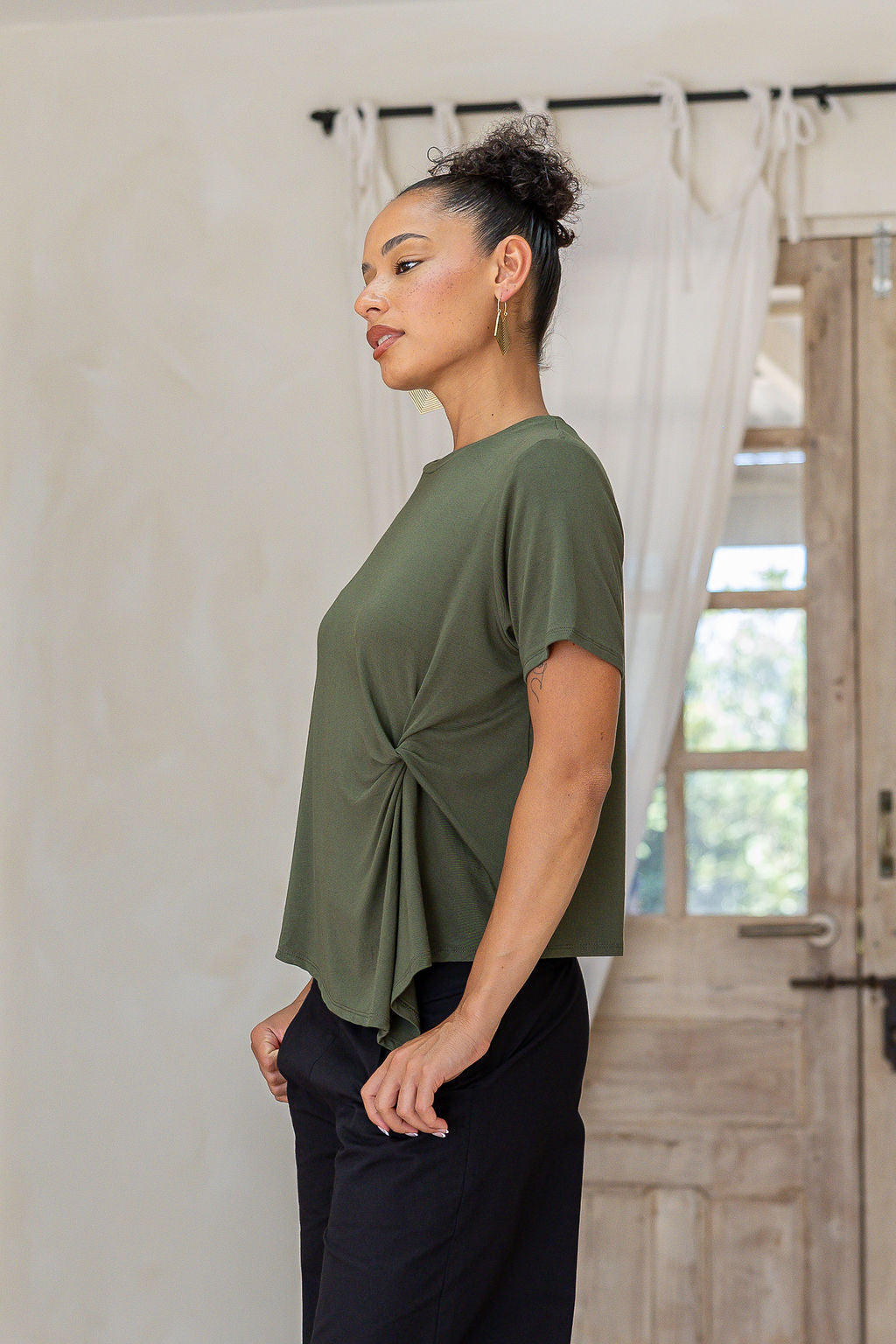 Woman wearing a soft stretch rayon T-shirt in olive green with a twist knot front, styled with black cotton pants