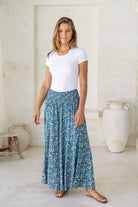 Woman wearing a white stretch top with 100% rayon wide legged flowy pants in blue based floral print with smocked elastic waistband.