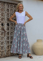 Woman standing infront of a wooden door wears 100% rayon wide leg pants in duck egg based floral print with white and pink highlights