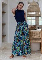 A woman modelling a sleeveless navy blue mock neck top with multicoloured floral and peacock print ultra wide leg rayon pants