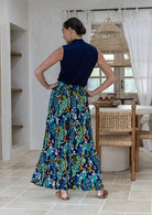 A woman shown from the back wearing a sleeveless navy top and ultra wide rayon pants with a wide shirred waistband in a multicolour floral and peacock print
