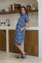 Woman standing sideways wearing a 100% cotton relaxed fit collared short sleeve dress with hidden side pockets. 