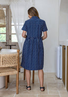 Woman standing backwards wearing a 100% cotton relaxed fit collared short sleeve dress with hidden side pockets.