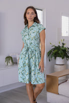 Model posing wears 100% cotton floral print shirt style dress with cap sleeves, fabric waist tie and box pleats at the waist.