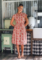 Woman wears fit and flare style shirt dress, 100% cotton with collar, cap sleeves, and removable waist tie in gentle cream based floral print.