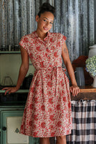 Model posing wears 100% cotton floral print shirt style dress with cap sleeves, fabric waist tie and box pleats at the waist.