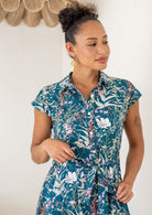 close up of woman wearing the Ursula Dress fit and flare style in Verdure, a teal cotton shirt dress with wildflower print 