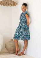 Side view of woman wearing the Ursula Dress fit and flare style in Verdure, a teal cotton shirt dress with wildflower print 