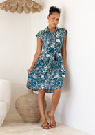 Woman wearing a cotton floral dress standing in a room with a textured wall and woven basket.