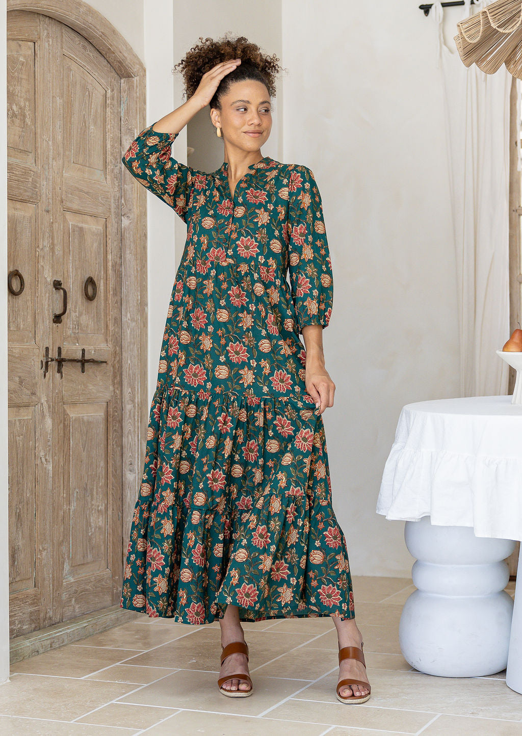 Woman wearing a green floral cotton dress with sleeves standing in a room with wooden door
