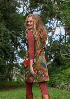 Woman wearing a moss green based multi-coloured floral print cotton velvet sleeveless tunic standing in a natural settings.