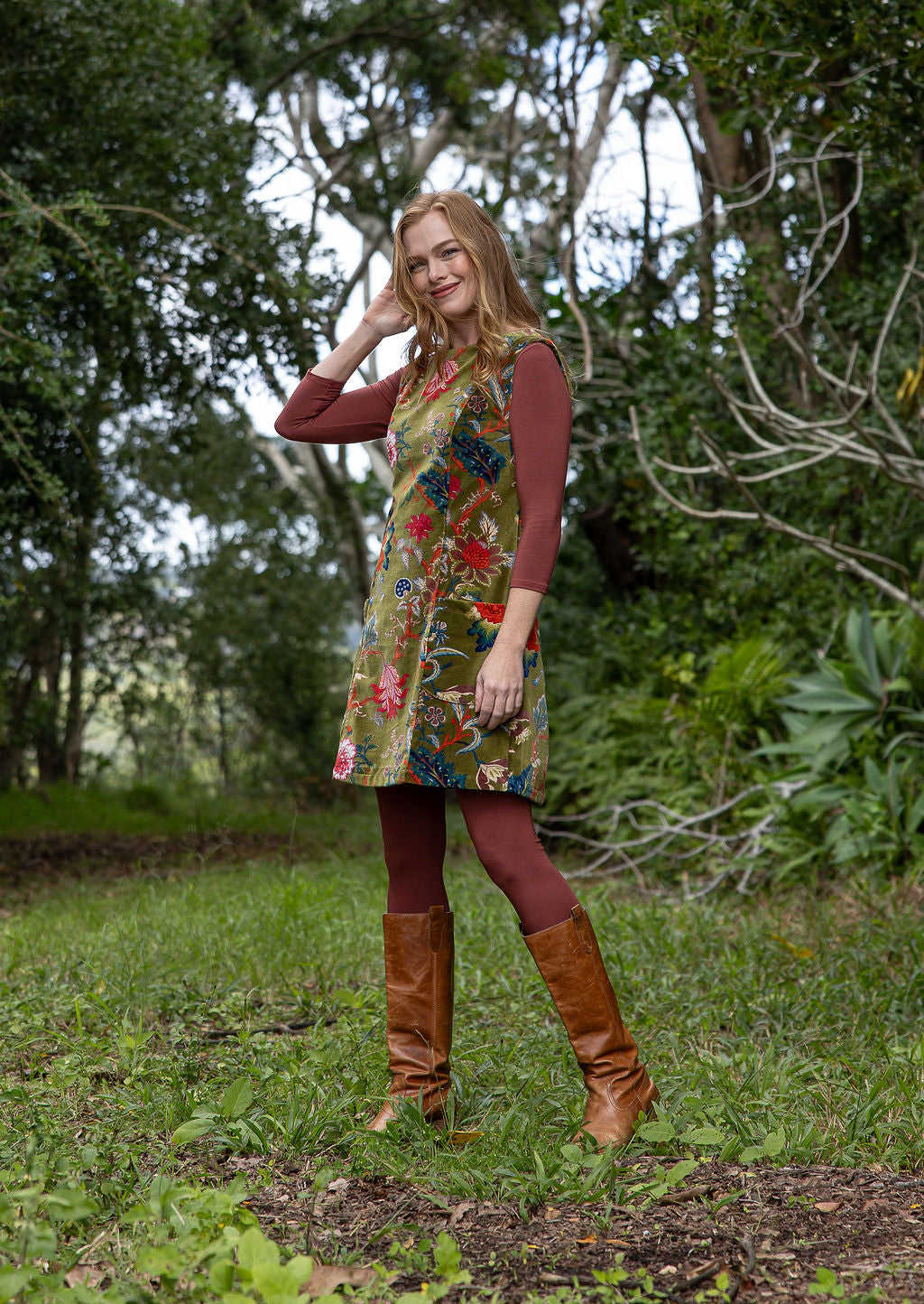 Woman in a cotton velvet floral dress and brown boots standing in a forest