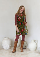 Woman wearing a green based multi-coloured floral cotton velvet tunic over a leggings and a basic top with brown boots. 