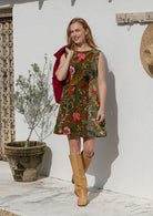 Woman standing wearing a cotton velvet sleeveless tunic in a green based multi-coloured floral print with cord jacket