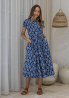 Woman wears retro style cotton button through midi length dress with high round neckline, short sleeves and a removable waist tie.