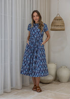 Woman wears 100% cotton button through midi length dress with short sleeves and pockets in floral print on a navy base