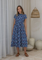 Woman in a floral dress standing in front of a white curtains.