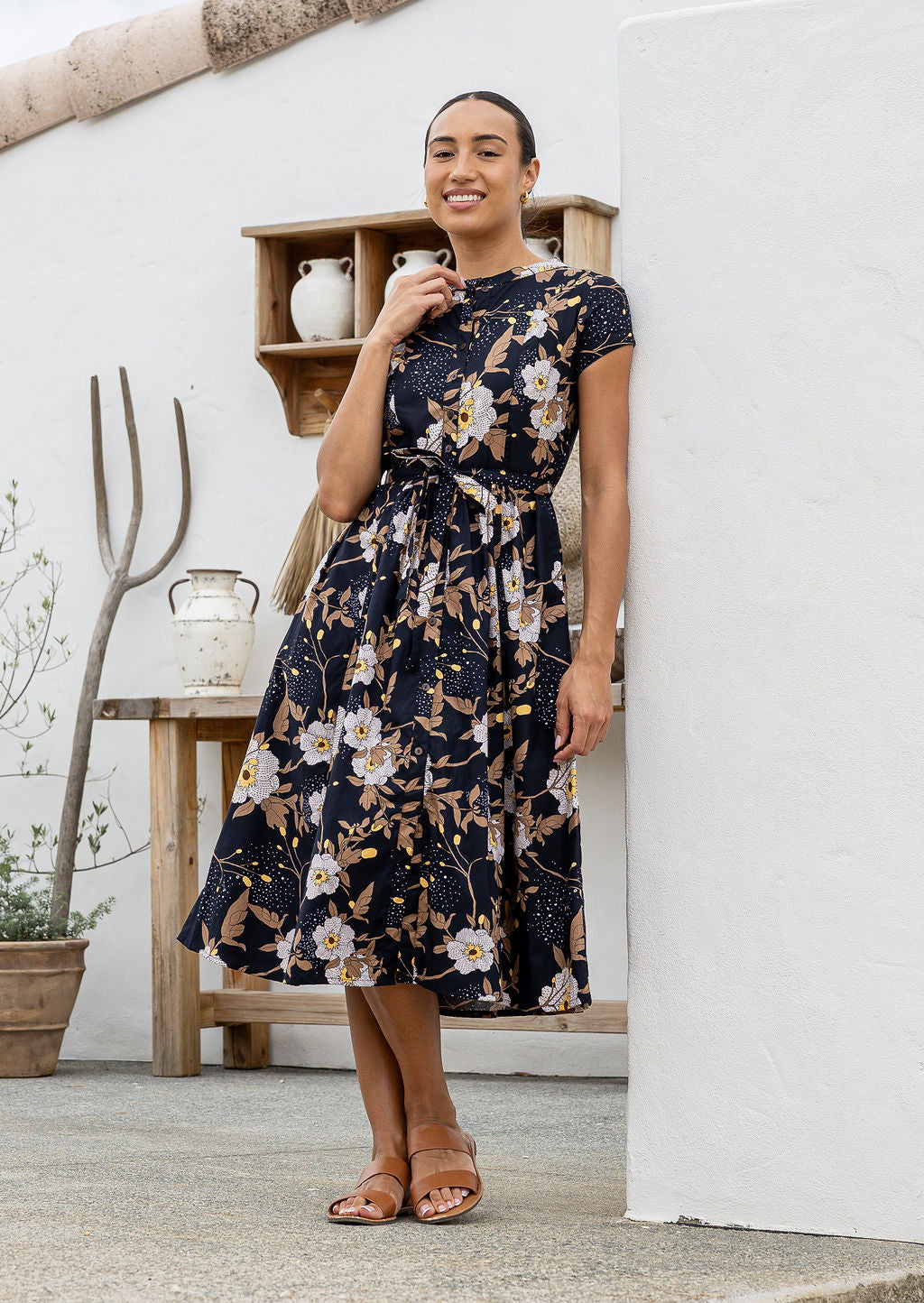 Woman wears retro style cotton button through midi length dress with high round neckline, short sleeves and a removable waist tie.