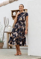Woman wears retro style cotton button through midi length dress with high round neckline, short sleeves and a removable waist tie.