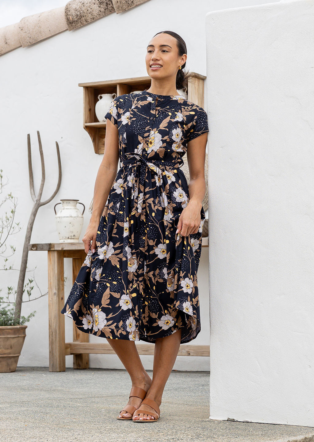 Woman poses in 1950's style short sleeved, button through cotton dress with high round neckline in black based floral print.