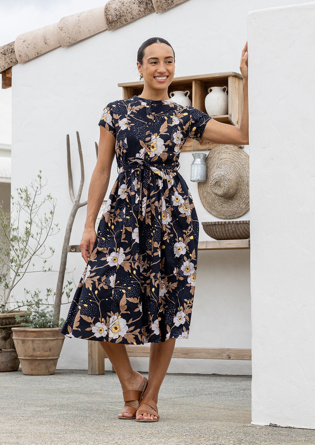 Woman wears 100% cotton button through midi length dress with short sleeves and pockets in floral print on a black base.