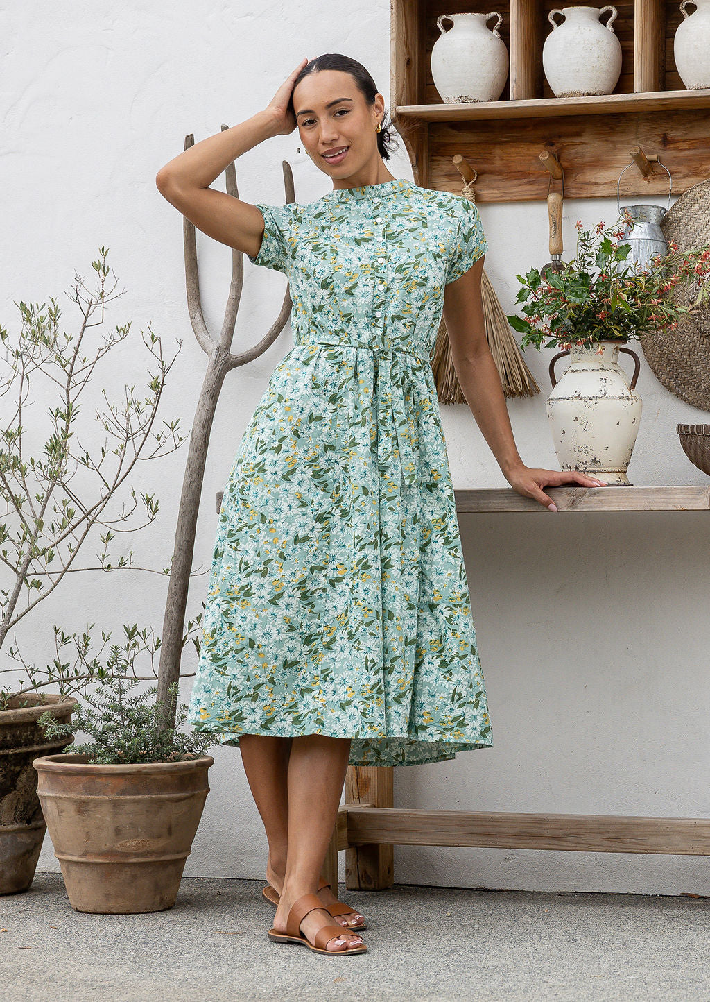 Woman wears 100% cotton button through midi length dress with short sleeves and pockets in floral print on a sage green base.