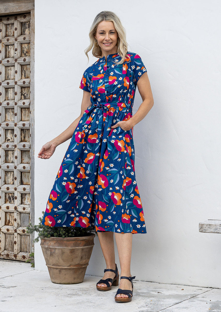 Woman wears retro style cotton button through midi length dress with high round neckline, short sleeves and a removable waist tie.