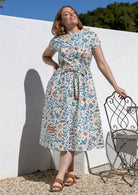 Woman wears retro style cotton button through midi length dress with high round neckline, short sleeves and a removable waist tie.