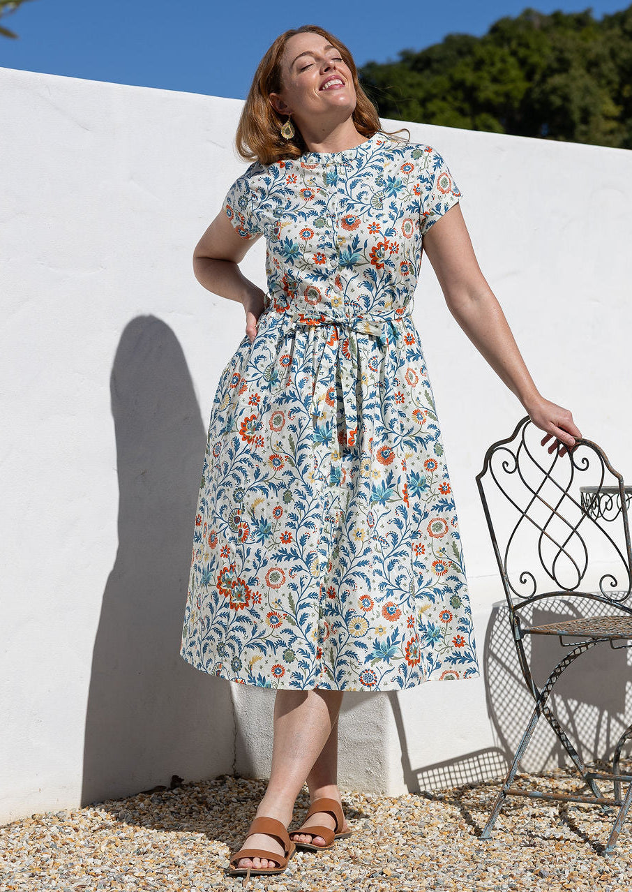 Woman wears retro style cotton button through midi length dress with high round neckline, short sleeves and a removable waist tie.