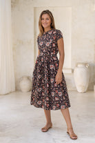 Woman wears retro style cotton button through midi length dress with high round neckline, short sleeves and a removable waist tie.