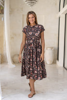 Woman wears 100% cotton button through midi length dress with short sleeves and pockets in indian floral print on a black base.