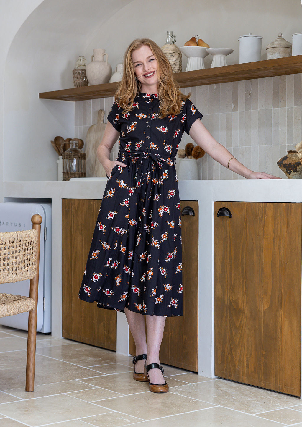 Woman wears 100% cotton button through midi length dress with short sleeves and pockets in floral print on a black base.