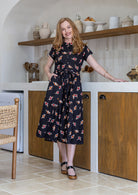 Woman wears 100% cotton button through midi length dress with short sleeves and pockets in floral print on a black base.