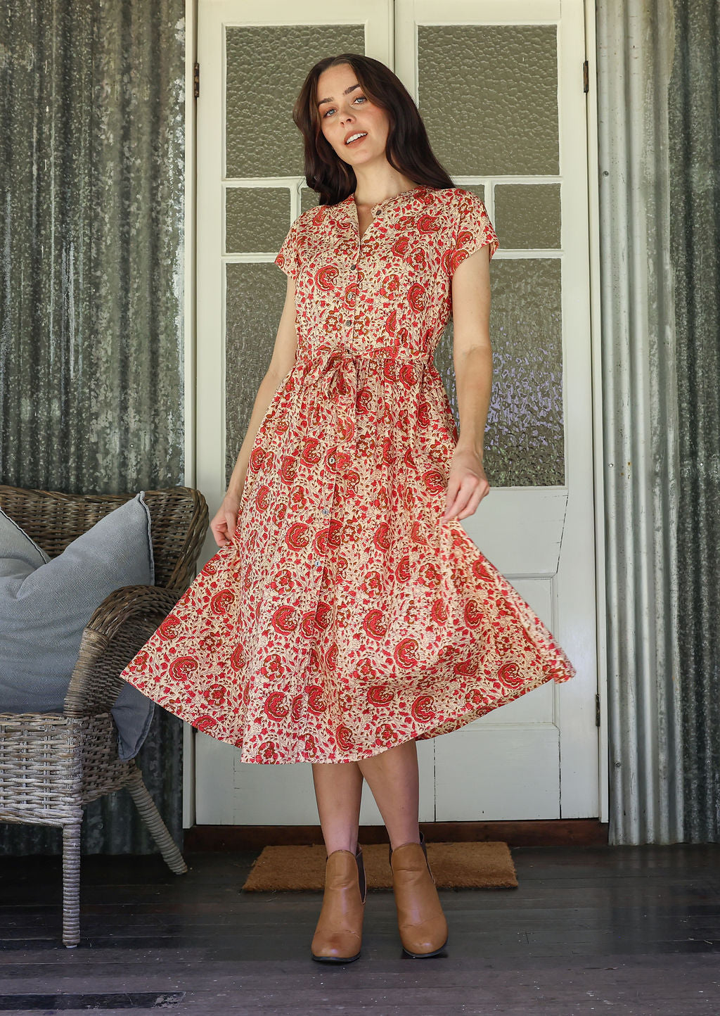 Woman wearing a floral dress standing in a room with wicker furniture and patterned walls.