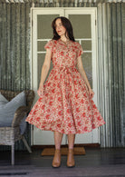 Woman wears 100% cotton button through midi length dress with short sleeves and pockets in floral print on a gentle cream base.