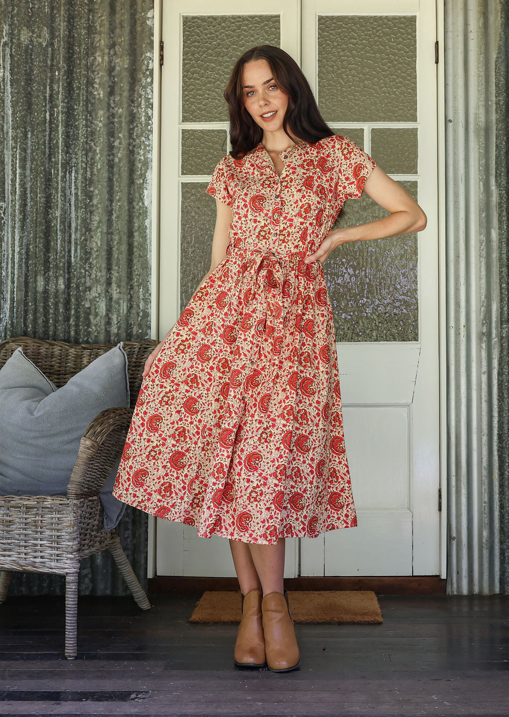 Woman wears retro style cotton button through midi length dress with high round neckline, short sleeves and a removable waist tie.
