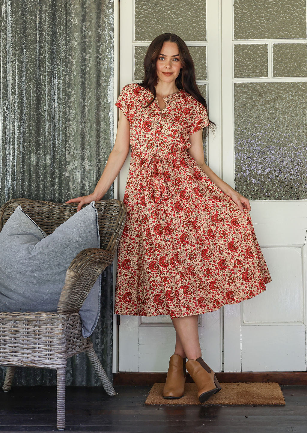 Woman  wearing a gentle cream based floral printed cotton button through cotton dress with hidden side pockets, short sleeves and a detachable waist tie.