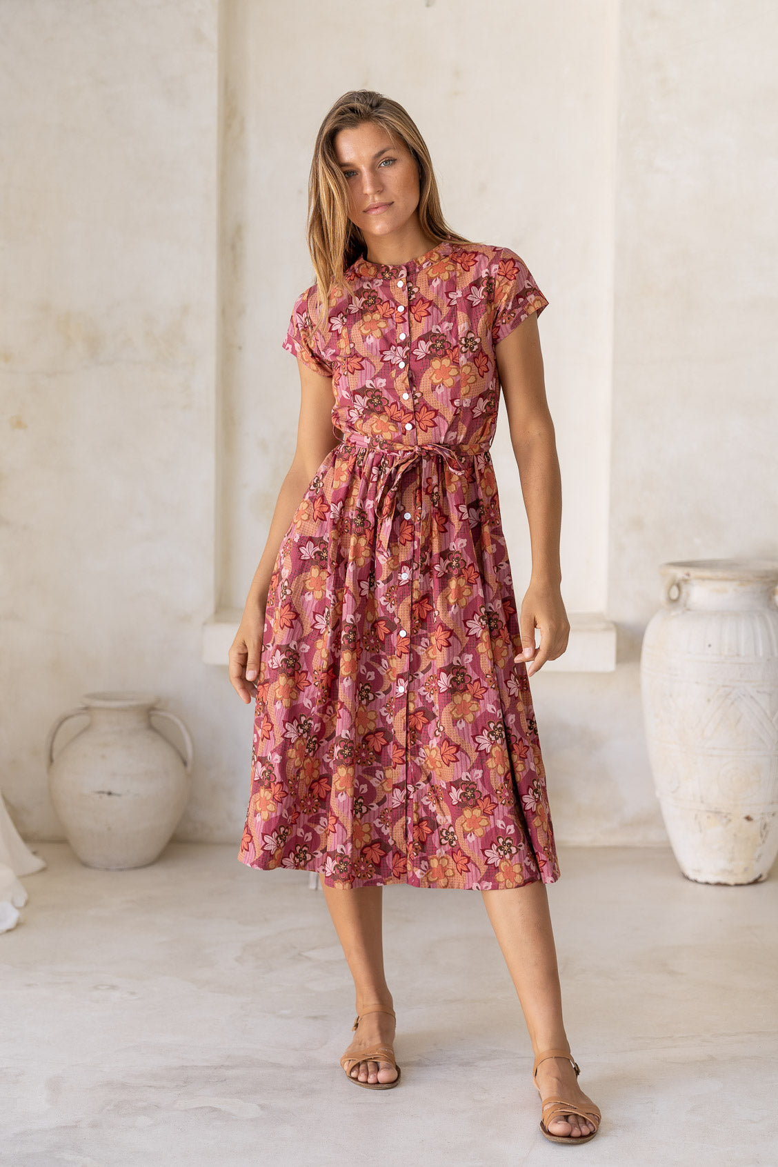 Woman wears 50's style cotton button through midi length dress with high round neckline, short sleeves and a waist tie in a japanese style floral print.