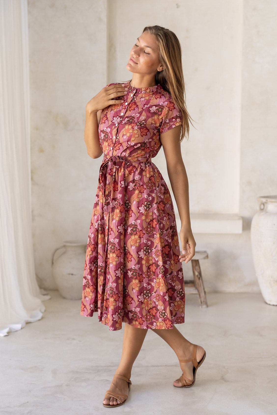 Woman poses in cotton 50's style midi length dress with short sleeves, pockets and a detachable waist tie.