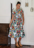 Woman wears retro style cotton button through midi length dress with high round neckline, short sleeves and a removable waist tie.