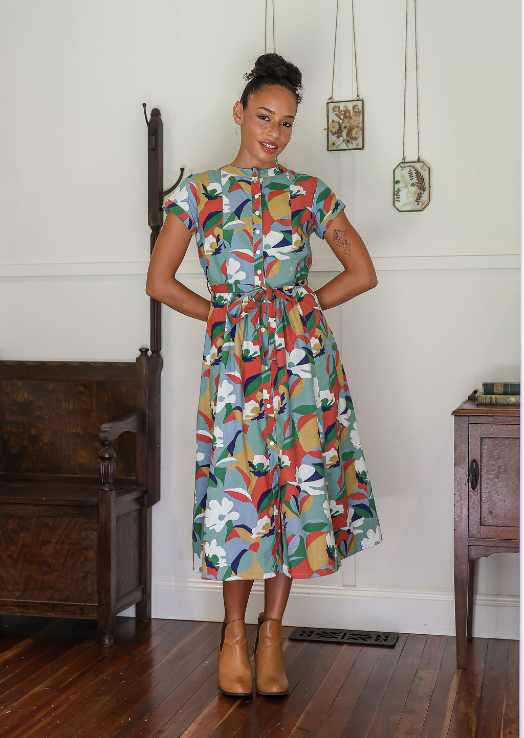 Woman wearing a colourful floral printed cotton button through cotton dress with hidden side pockets, short sleeves and a detachable waist tie.