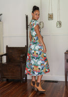 Woman stands sideways wearing a colourful floral printed cotton button through cotton dress with hidden side pockets.