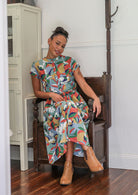 Woman in a colorful dress sitting on a wooden chair in a room.